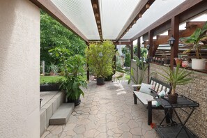 Un patio couvert avec un sol en pierre, un banc en bois, des plantes en pot et une table en métal.