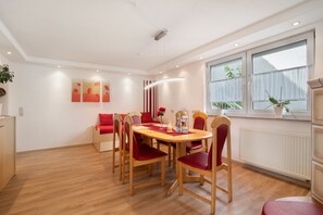 A dining area with a round table, red chairs, and a window with plants.