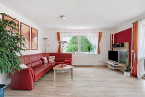 A modern living room with a red sofa, a coffee table, a TV, and a large window with curtains.