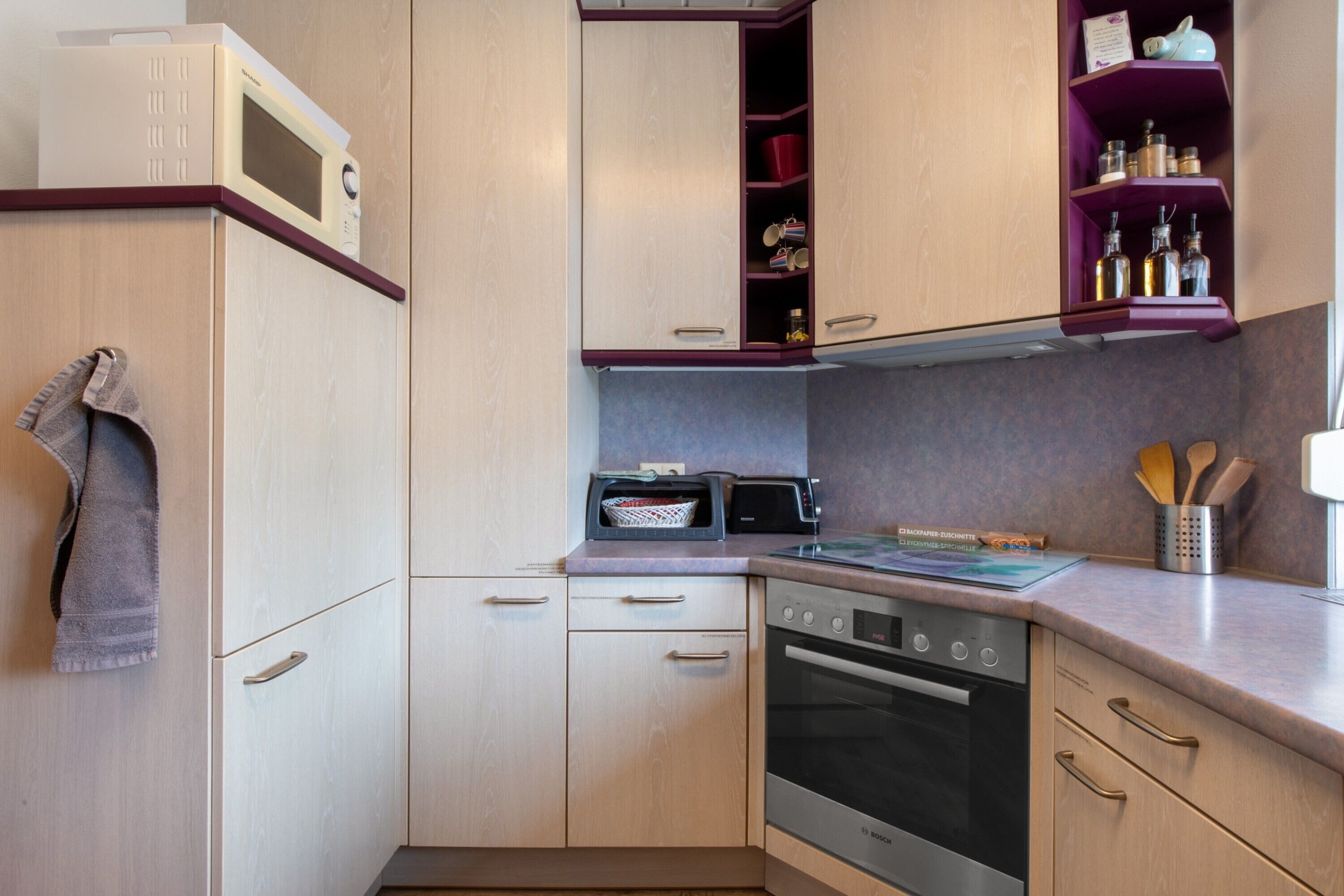 A compact kitchen with a microwave, toaster, oven, and a shelf with kitchen utensils.