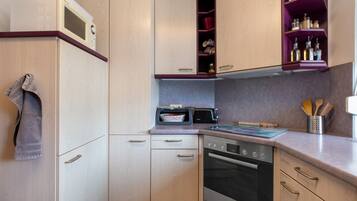 Een compacte keuken met een magnetron, broodrooster, oven en een plank met keukengerei.