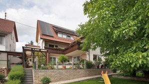 Una propiedad residencial con un muro de contención de piedra, un patio cubierto de césped, un tobogán amarillo y una casa con techo de tejas y paneles solares.