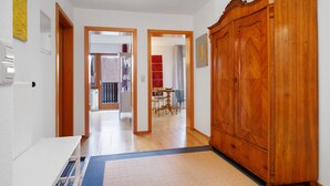 A hallway with a wooden wardrobe, a white desk, and a dining area in the background. - Apartment 'Birkach 35' with Balcony and Wi-Fi (Lindau am Bodensee)