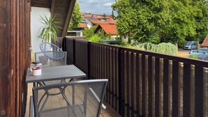 A balcony with a table and chairs, a hanging lantern, and a view of houses and trees. - Apartment 'Birkach 35' with Balcony and Wi-Fi (Lindau am Bodensee)
