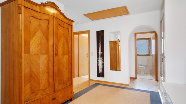 A hallway with a wooden wardrobe, a black vertical artwork, a mirror, and an arched doorway leading to a bathroom.