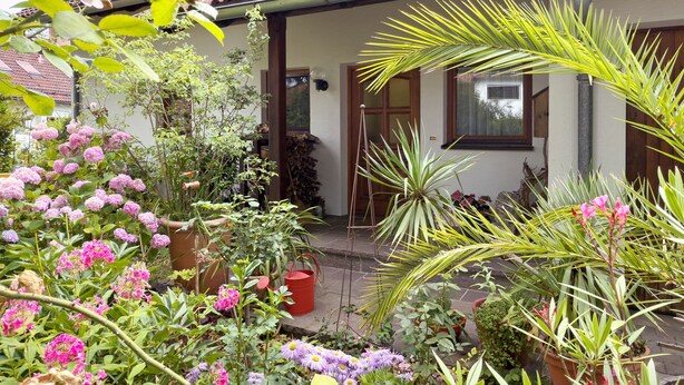 A house with a tiled roof, a garden with various plants and flowers, and a wooden door. - Apartment 'Birkach 35' with Balcony and Wi-Fi (Lindau am Bodensee)