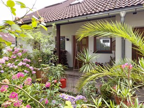 Une maison avec un toit en tuiles, un jardin avec différentes plantes et fleurs, et une porte en bois.