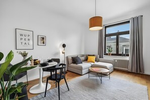 A modern living room with a dining area, a sofa, a coffee table, a hanging light fixture, and a large window with curtains. - Apartment 'Top Wohnung-neu-20 Min Nach Dus' with Wi-Fi (Wuppertal)