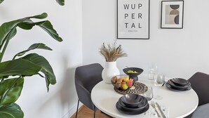 Un comedor con una mesa redonda, sillas negras, un jarrón blanco con plantas secas, un frutero y platos negros.