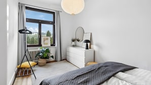 Un dormitorio con cama, cómoda, espejo, planta en maceta y ventana con cortinas.
