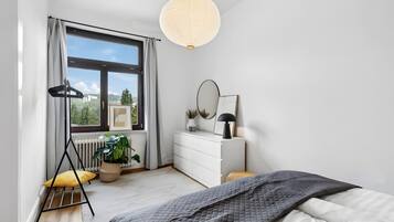 Ein Schlafzimmer mit Bett, Schminktisch, Spiegel, Zimmerpflanze und einem Fenster mit Vorhängen.