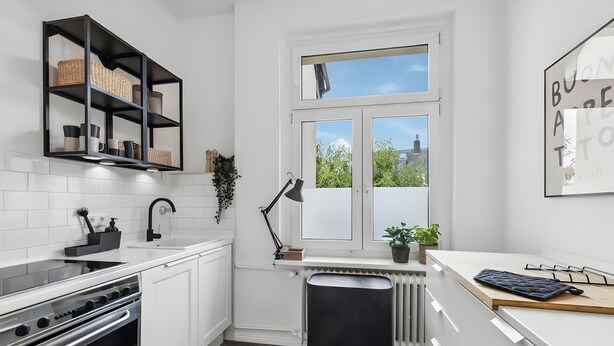 Una cocina moderna con armarios blancos, una campana extractora negra, horno empotrado, lavavajillas negro y una ventana con vistas a la vegetación.