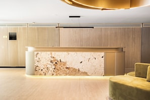 Een moderne receptie met een marmeren balie, houten paneelwanden en een gele bank.