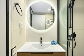 Een moderne badkamer met een witte wastafel, een ronde spiegel en een douche met glazen wanden.