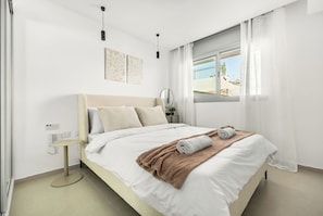 Een moderne hotelkamer met een groot bed, een nachtkastje, een klein rond tafeltje, een raam met gordijnen en uitzicht op buiten.