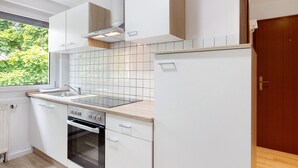 A modern kitchen with white cabinetry, a built-in oven, and a window with a view of greenery.