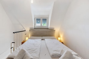 A bedroom with a bed, a window with blinds, a headboard, and bedside lamps.