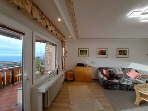 Un salon comprenant un canapé, une petite table, un radiateur et une fenêtre donnant sur un balcon.