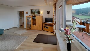 Ein modernes Wohnzimmer mit einem Holzkabinett, einem Flachbildfernseher und einem Balkon mit Blick auf die Landschaft.