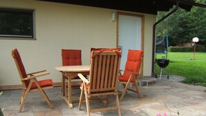 An outdoor patio with a table and four chairs, a barbecue grill, and a door.