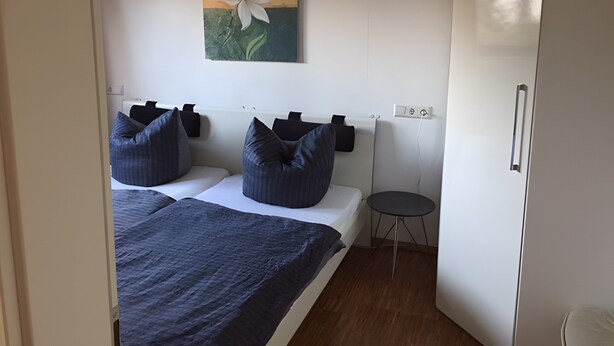 A bedroom with a bed, pillows, a small table, a wall-mounted painting, and a wardrobe.