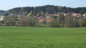 A rural village with houses on a hillside, a clear sky, and a green field in the foreground.