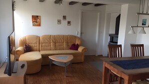 A living room with a sofa, a coffee table, a dining table with chairs, a TV, and a fireplace.