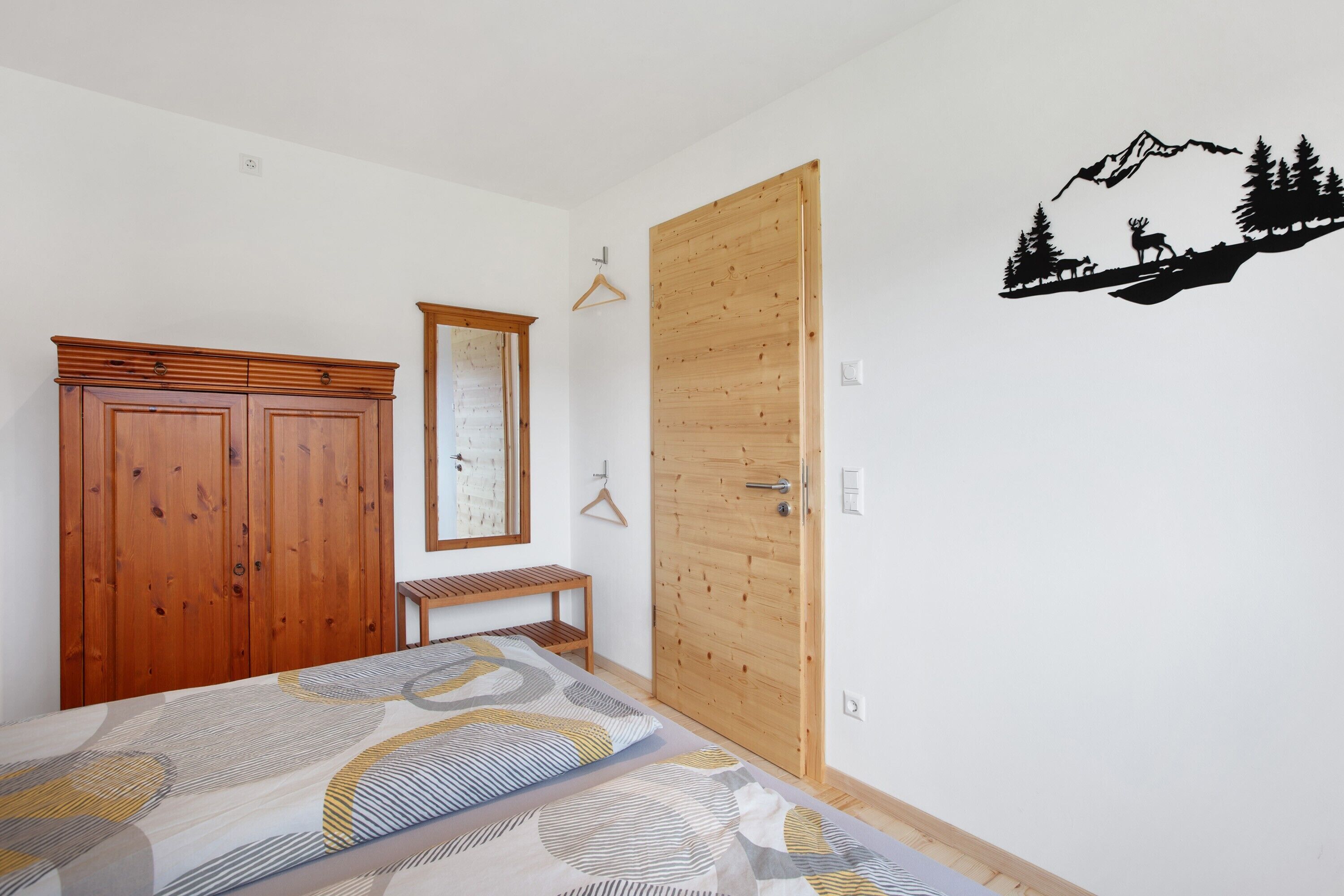 A bedroom with a bed, wooden wardrobe, a bench, a door, and a wall decal.