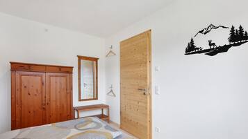A bedroom with a bed, wooden wardrobe, a bench, a door, and a wall decal.