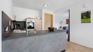 A modern kitchen with a central island, built-in oven, and a wooden door leading to another room.
