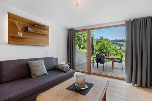 A modern living room with a sofa, a glass table with a candle, and a view of an outdoor patio.