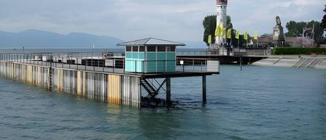 A pier extending into calm water with a lighthouse in the background and a statue on a platform.