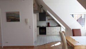 Eine Küche mit weißen Schränken, einem Herd und einem roten Gerät. Es gibt einen Esstisch mit Stühlen und ein Bild an der Wand.