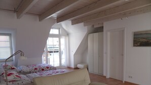 Ein Schlafzimmer mit Bett, Sofa, Schreibtisch, Lampe, Fenster und Tür.