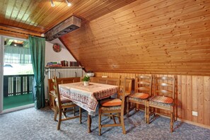 Un coin repas avec une table dressée pour quatre personnes, des chaises en bois, un rideau vert et une vue sur un balcon.