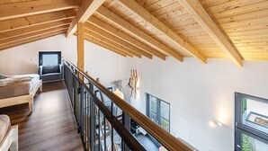 A high-ceilinged room with wooden beams, a staircase, a bed, and a view through a window. - Apartment 'Sonnenwind Am Hainer See' with Lake View and Wi-Fi (Neukieritzsch)