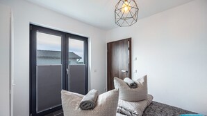 Een hotelkamer met een grote schuifdeur naar een balkon, een bed met beddengoed met een patroon, en een geometrische lamp.