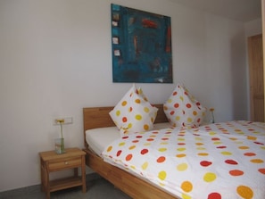 Un dormitorio con una cama, una mesita de noche, un florero con flores y un cuadro en la pared.