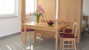 Une pièce avec une table à manger en bois, quatre chaises, un vase de fleurs et un lit à l’arrière-plan.