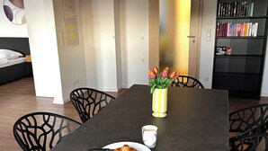 A dining area with a table, chairs, a vase of flowers, a plate with a croissant, and a cup of coffee. - Comfort-Apartment-93m²-Central-Near Stadtpark (Pfaffenhofen an der Ilm)