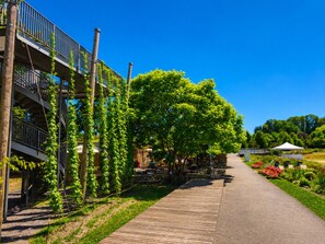 Een pad naar een gebouw met een balkon, omringd door groen en terrasmeubilair.