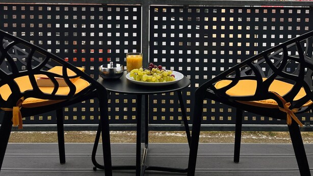 A balcony with two chairs and a table, a plate of grapes, a glass of orange juice, and a metal bowl. - Comfort-Apartment-93m²-Central-Near Stadtpark (Pfaffenhofen an der Ilm)