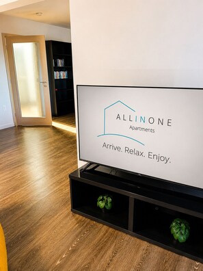 A sign for Allinone Apartments with a modern interior design, including a wooden floor and a bookshelf.