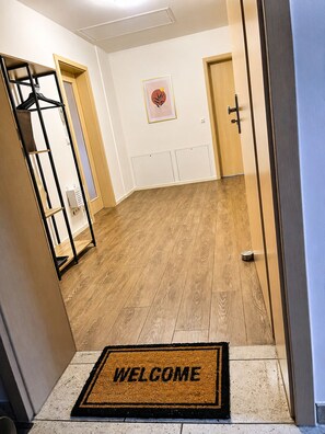 Un pasillo con piso de madera, un felpudo y una puerta con picaporte.