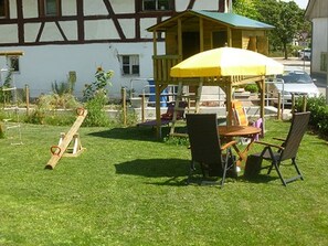 A wooden play structure with a yellow canopy, a swing set, and a table with chairs in a grassy yard.