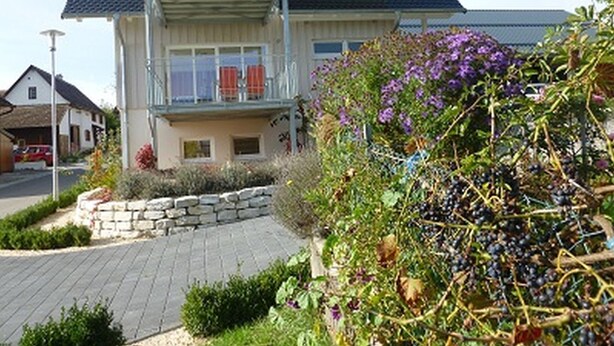 A two-story house with a balcony, a stone wall, and a garden with purple flowers. - Apartment 'Golden Delicious' with Shared Terrace, Shared Garden and Wi-Fi (Salem)