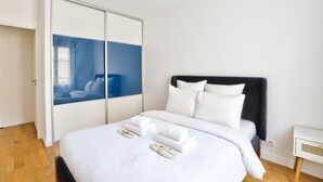 A neatly made bed with white linens and pillows, a black headboard, and a large wardrobe with sliding doors. - Puteaux - La défense - 2 chambres (Puteaux)