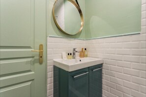 A bathroom with a white sink, a mirror, and a door with a gold handle. - 3. cosy 1BR - Père Lachaise - Nation (Paris)