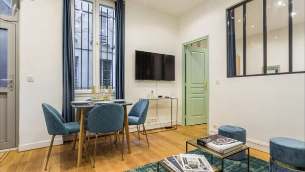A dining area with a table and chairs, a television mounted on the wall, and a green door. - 3. cosy 1BR - Père Lachaise - Nation (Paris)