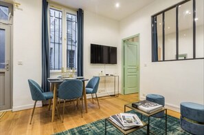 A dining area with a table and chairs, a television mounted on the wall, and a green door. - 3. cosy 1BR - Père Lachaise - Nation (Paris)